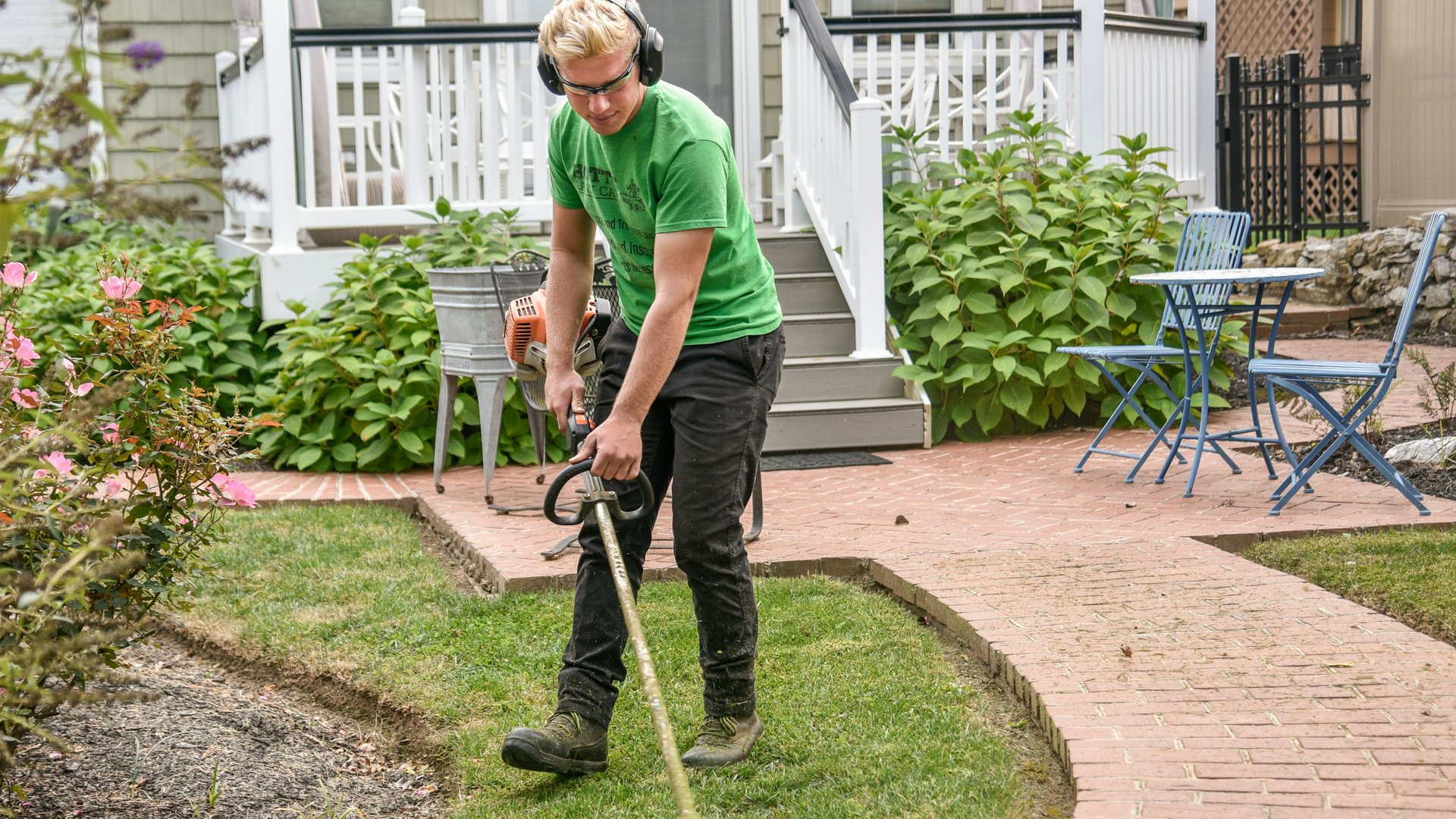 A landscaper trimming a lawn in a backyard